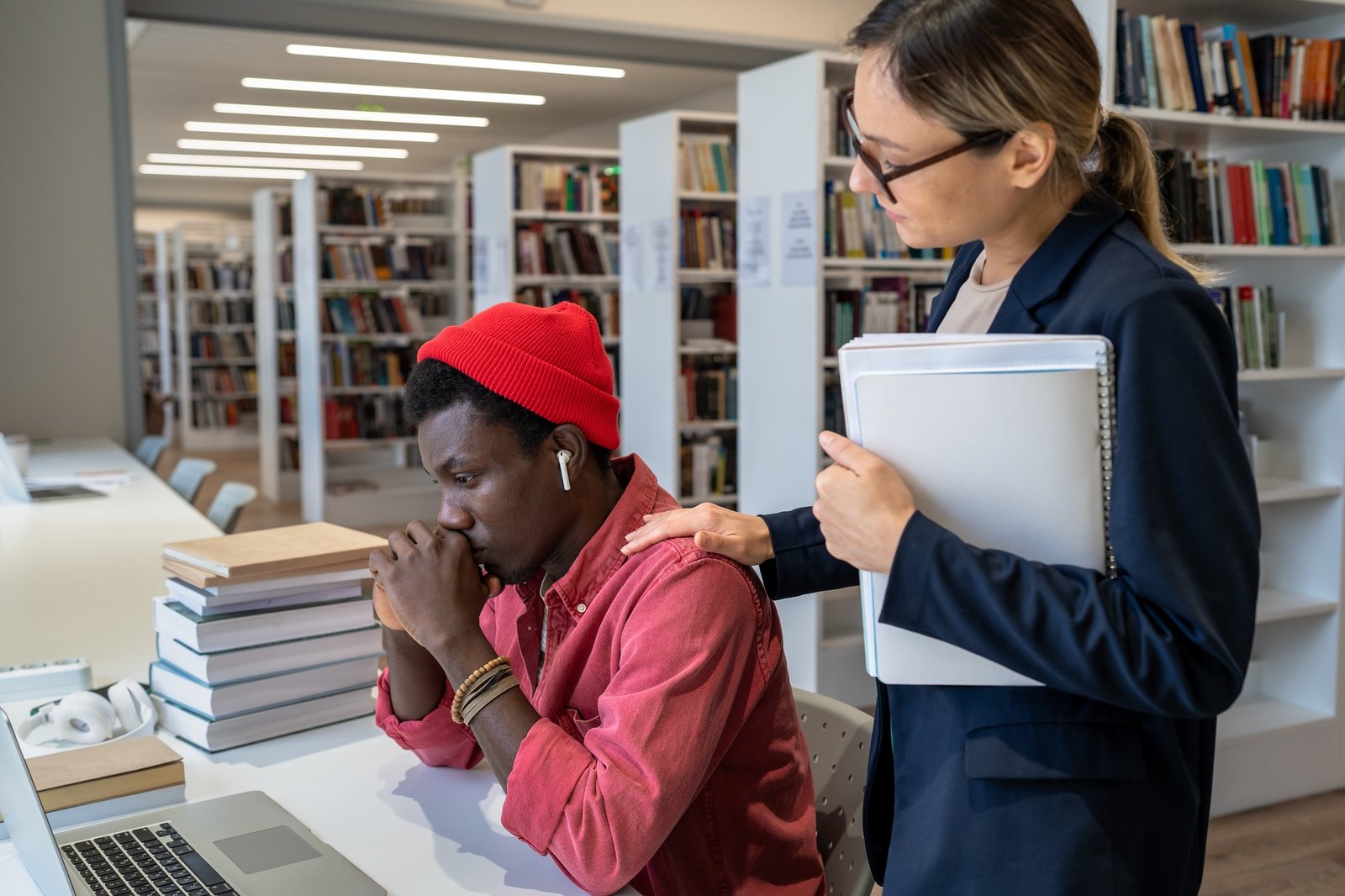 Young supportive woman teacher comforting and giving emotional support to upset student in library